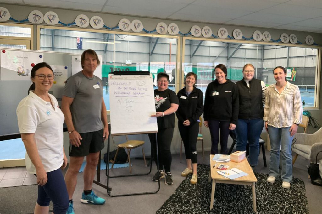 Two members of the Mood Active team with some program participants in a comfortable room, next to a whiteboard with lessons written on it.
